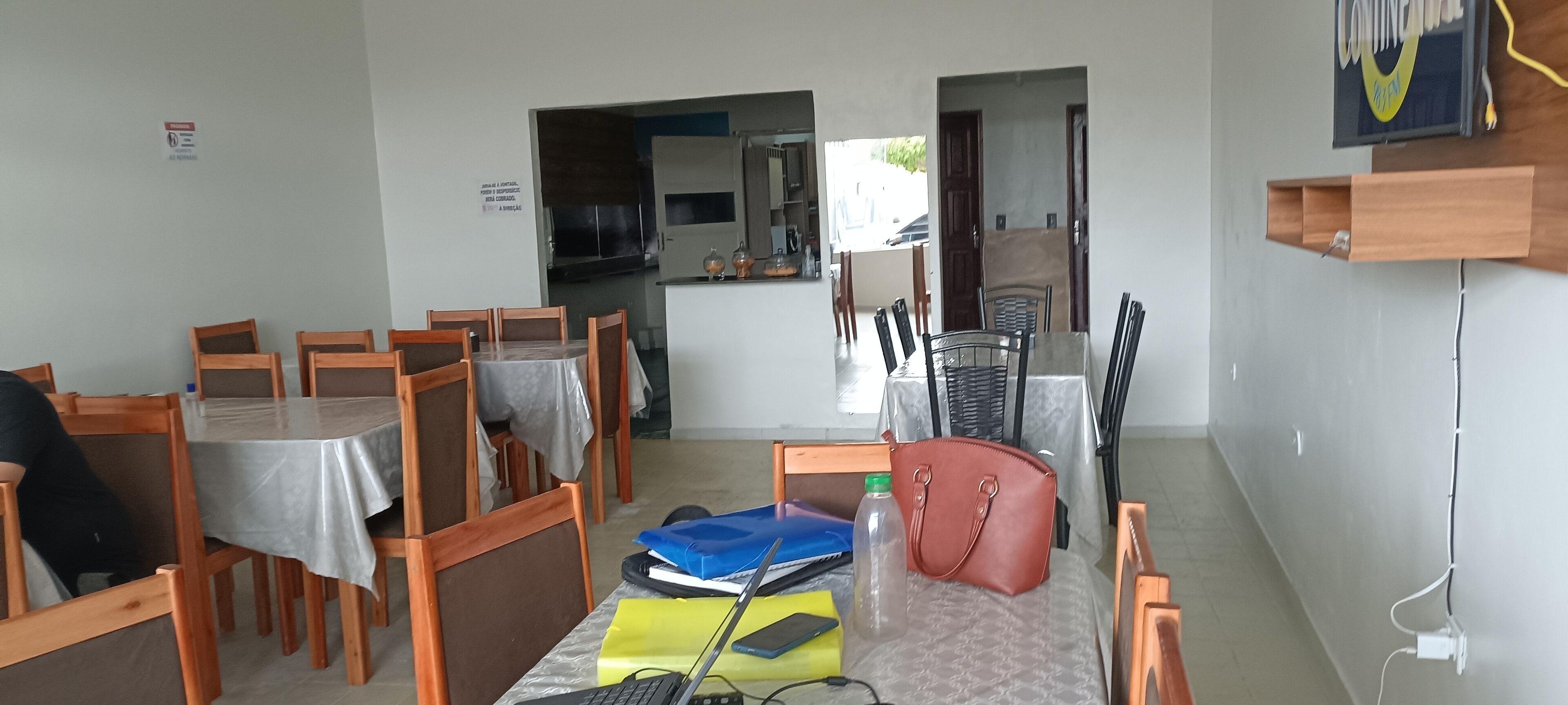A dining area with wooden tables and chairs, a kitchen in the background, and a small wooden shelf with a sign.