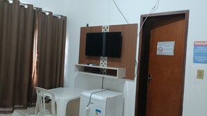 Ein Zimmer mit an der Holzvertäfelung montiertem Fernseher, einem kleinen weißen Schreibtisch mit Stuhl und einer Tür mit einem Schild.