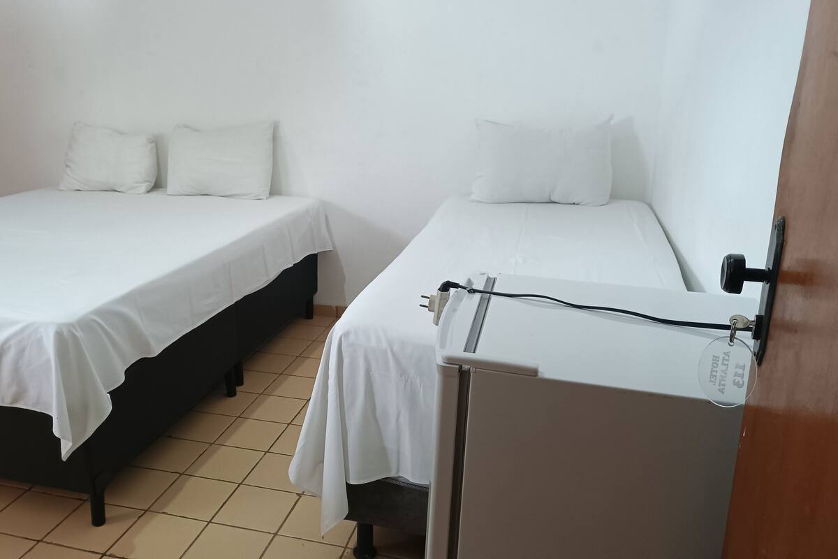 Ein Zimmer mit zwei Einzelbetten, jeweils mit weißer Bettwäsche und Kissen, einem Holzschrank und einem kleinen Tisch mit Steckdose.