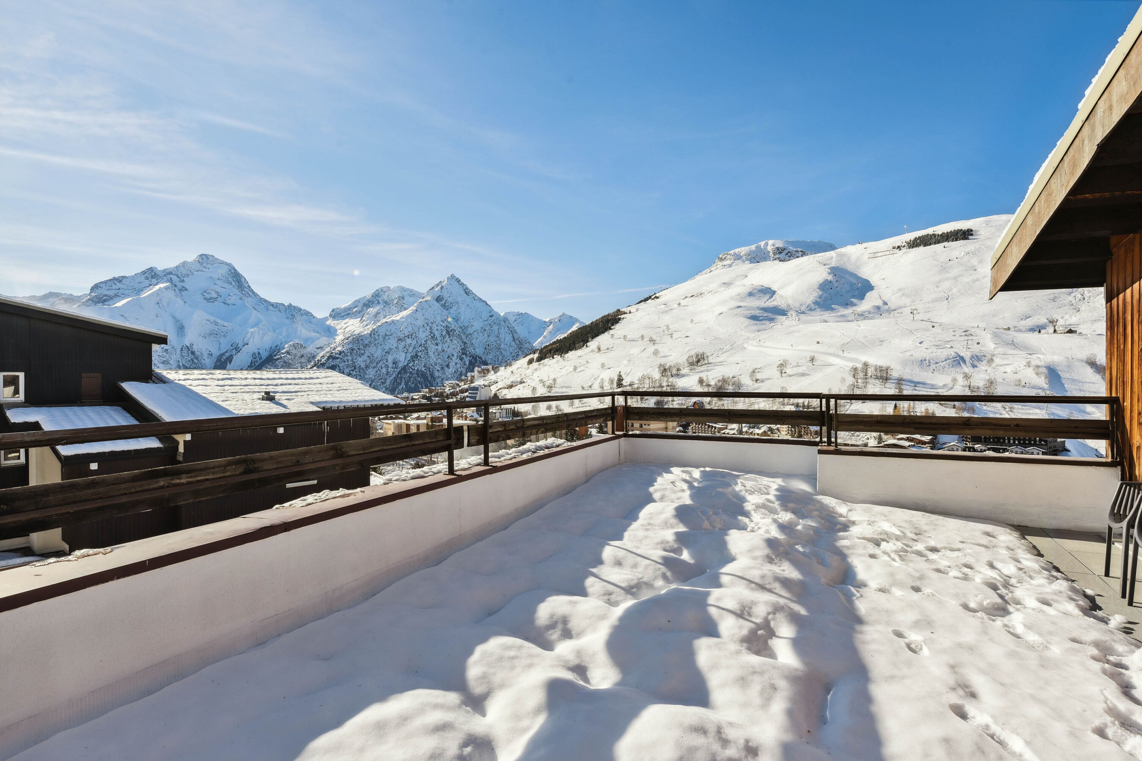 A snow-covered outdoor area with a wooden deck and a view of snow-capped mountains.