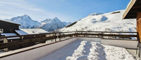 Un espacio exterior cubierto de nieve con una terraza de madera y vistas a montañas nevadas.