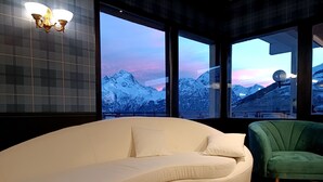 Un salon moderne avec un canapé blanc, un fauteuil vert et de grandes fenêtres donnant sur des montagnes enneigées.