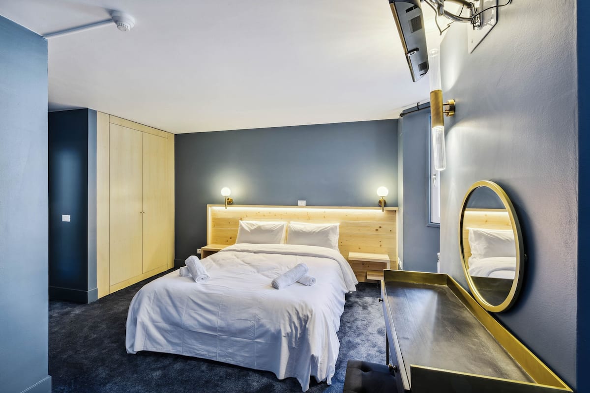 Ein ordentlich bezogenes Bett mit weißen Leinen und einem Handtuch, ein Holz-Kopfteil, ein Nachttisch und ein Spiegel an der Wand.