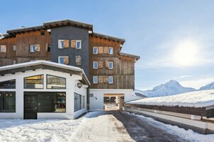 A multi-story building with a wooden facade and large windows, set against a snowy mountain backdrop.