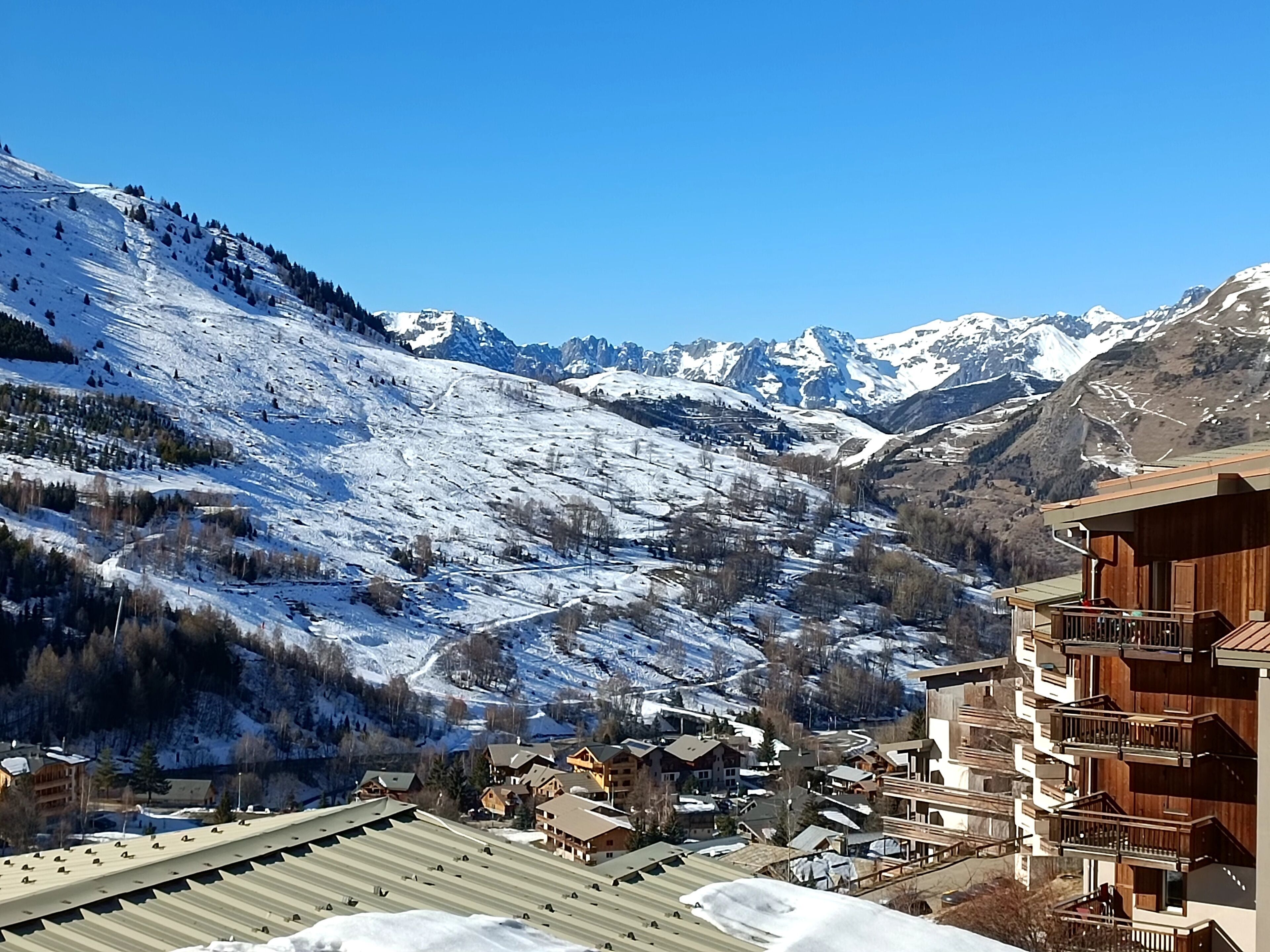 Un centro turístico de montaña con laderas nevadas, edificios de madera y un cielo azul despejado.