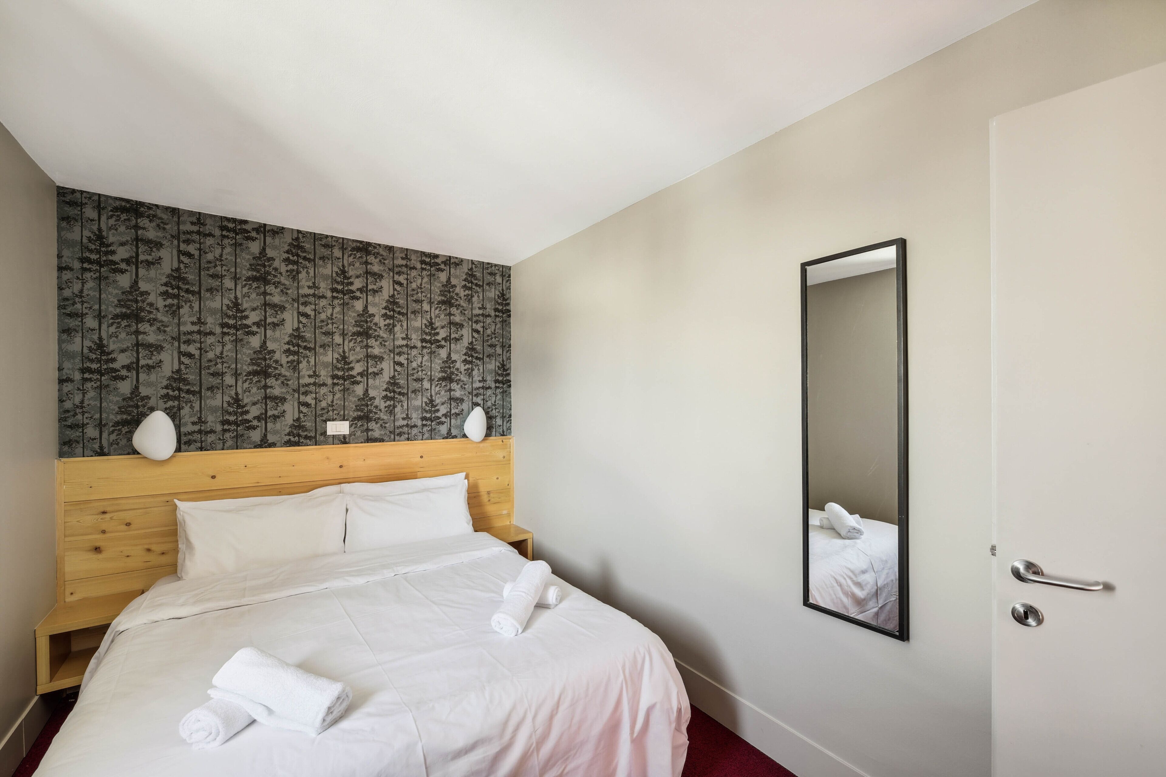 Habitación de hotel con cabecera de madera, un espejo grande y camas bien hechas con toallas.