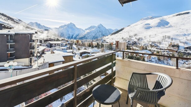 Un balcon donnant sur une ville de montagne enneigée, avec des balustrades en bois et deux chaises.