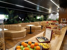 A modern lounge area with curved seating, a buffet with food and beverages, and a variety of plants.