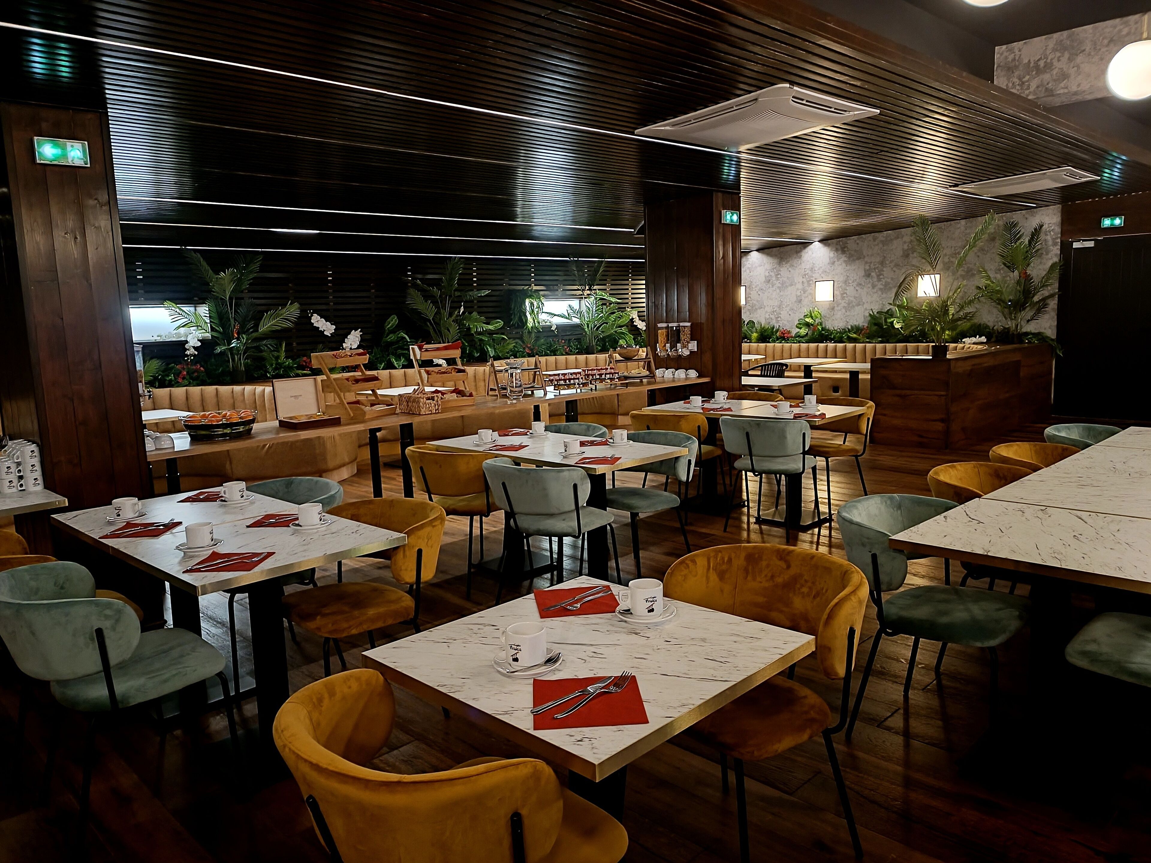 Un ristorante con diversi tavoli e sedie, elementi in legno e piante da interno.