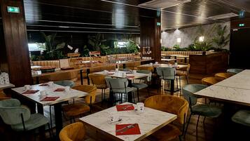Un ristorante con diversi tavoli e sedie, elementi in legno e piante da interno.