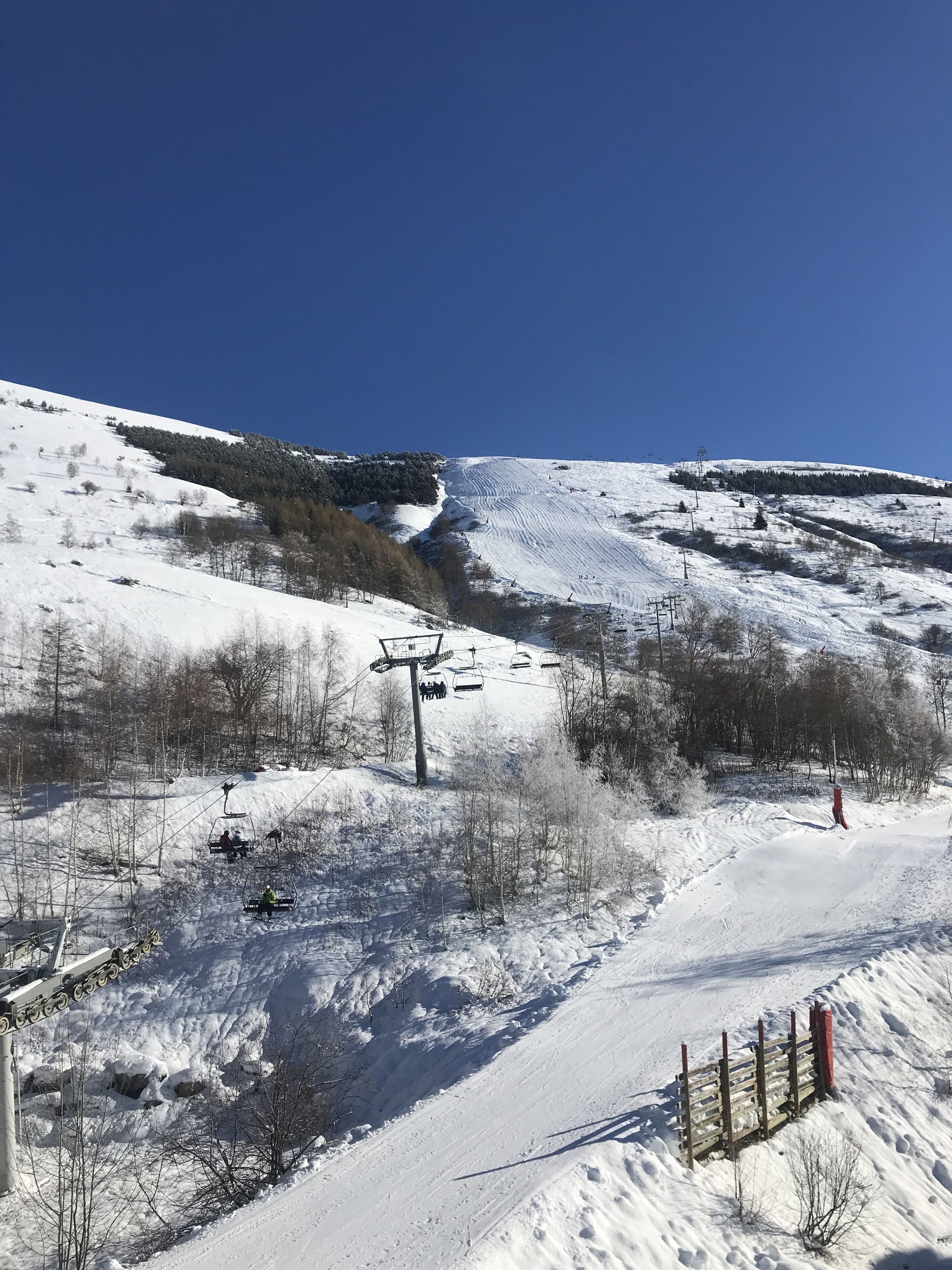 A snow-covered ski slope with ski lifts and a wooden fence.