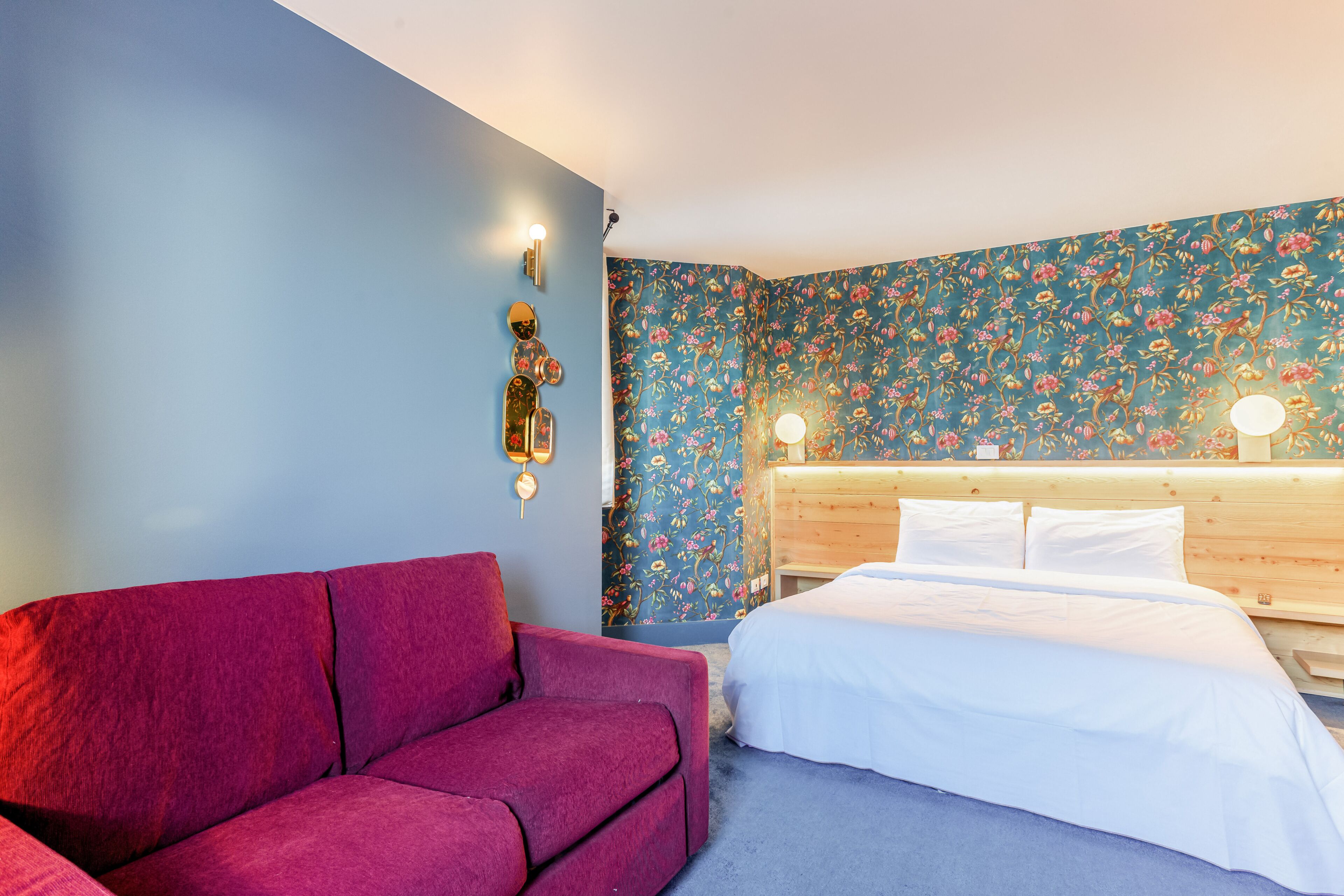 A room with a bed, a wooden headboard, a red sofa, and floral wallpaper.