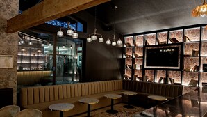 Un espace bar moderne avec un plafond en bois, un grand téléviseur mural et un coin salon doté de tables rondes et de chaises rembourrées.