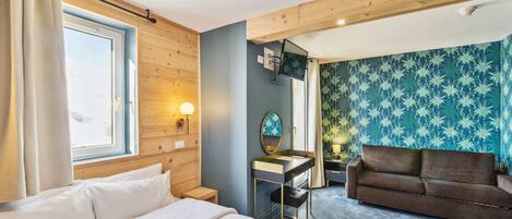 A hotel room with a bed, a desk, a sofa, and a large window.