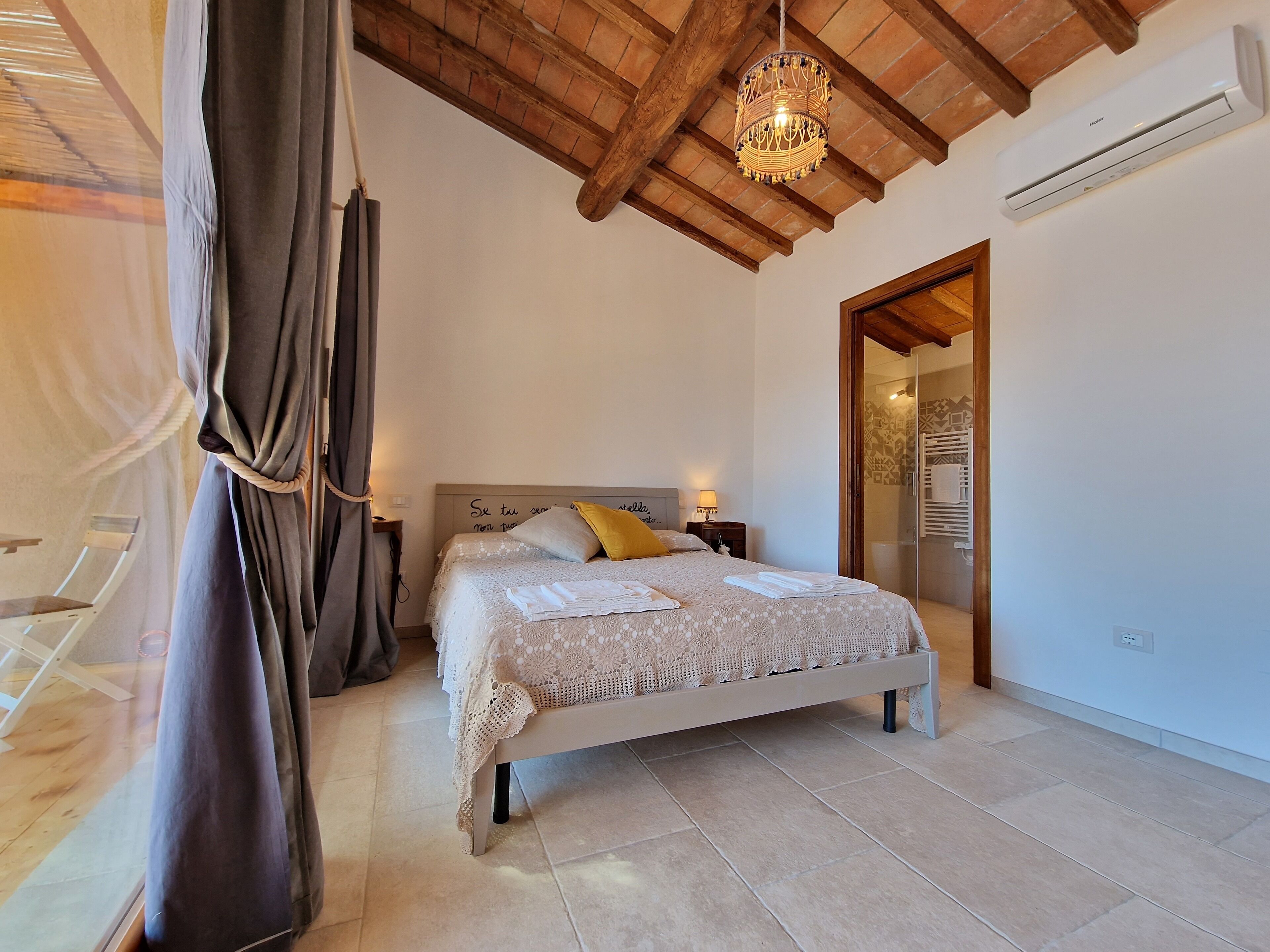 A bedroom with a bed, curtains, a chandelier, and an air conditioning unit.