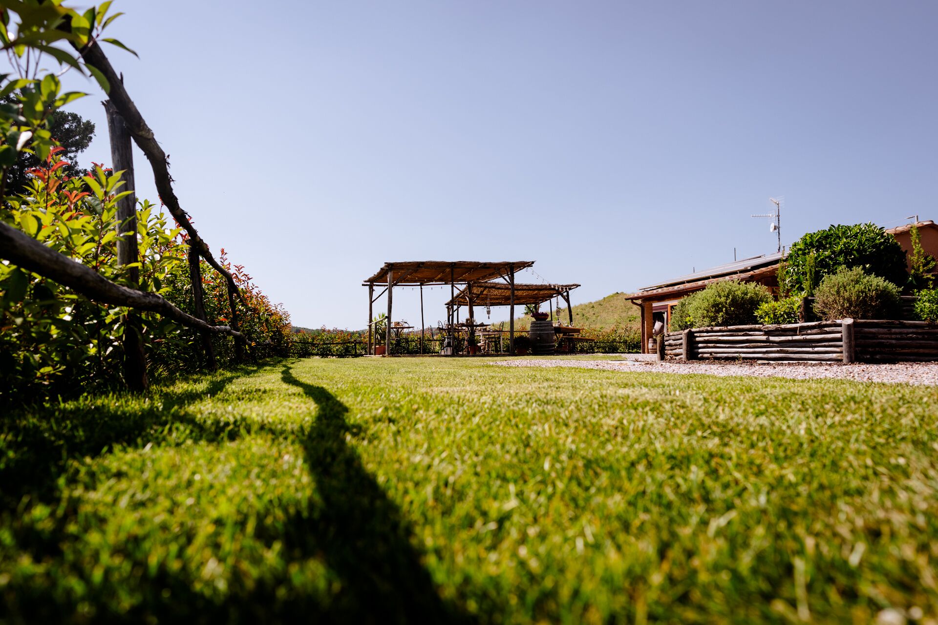 A rustic outdoor seating area with wooden tables and chairs, surrounded by a well-maintained lawn and greenery.