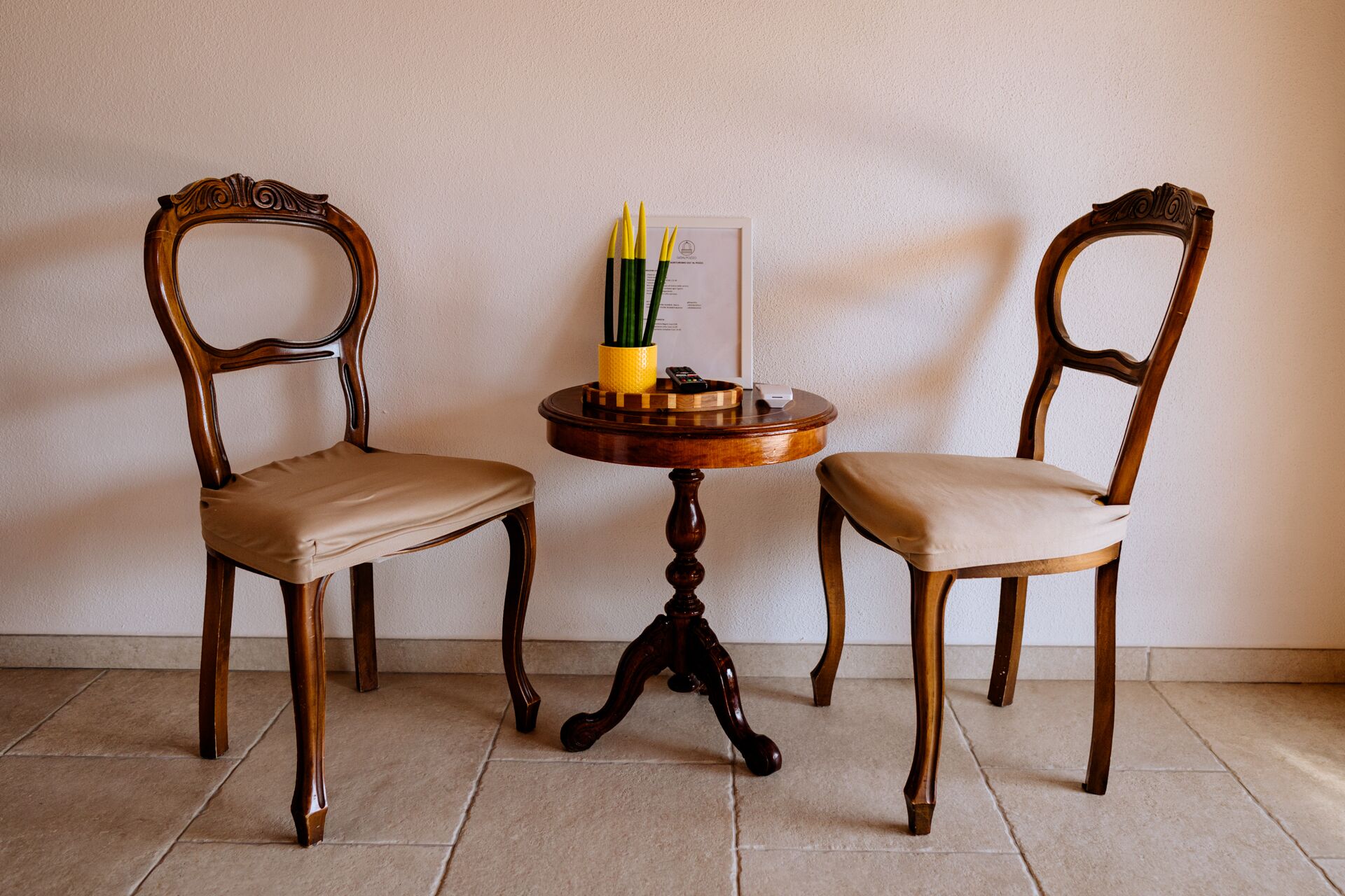 Dos sillas de madera con asientos y respaldos acolchados, ubicadas a ambos lados de una pequeña mesa redonda de madera con una bandeja.