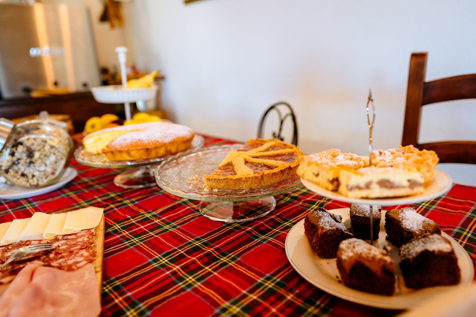 A table with various desserts and cheese, including pies and cakes, on a plaid tablecloth.