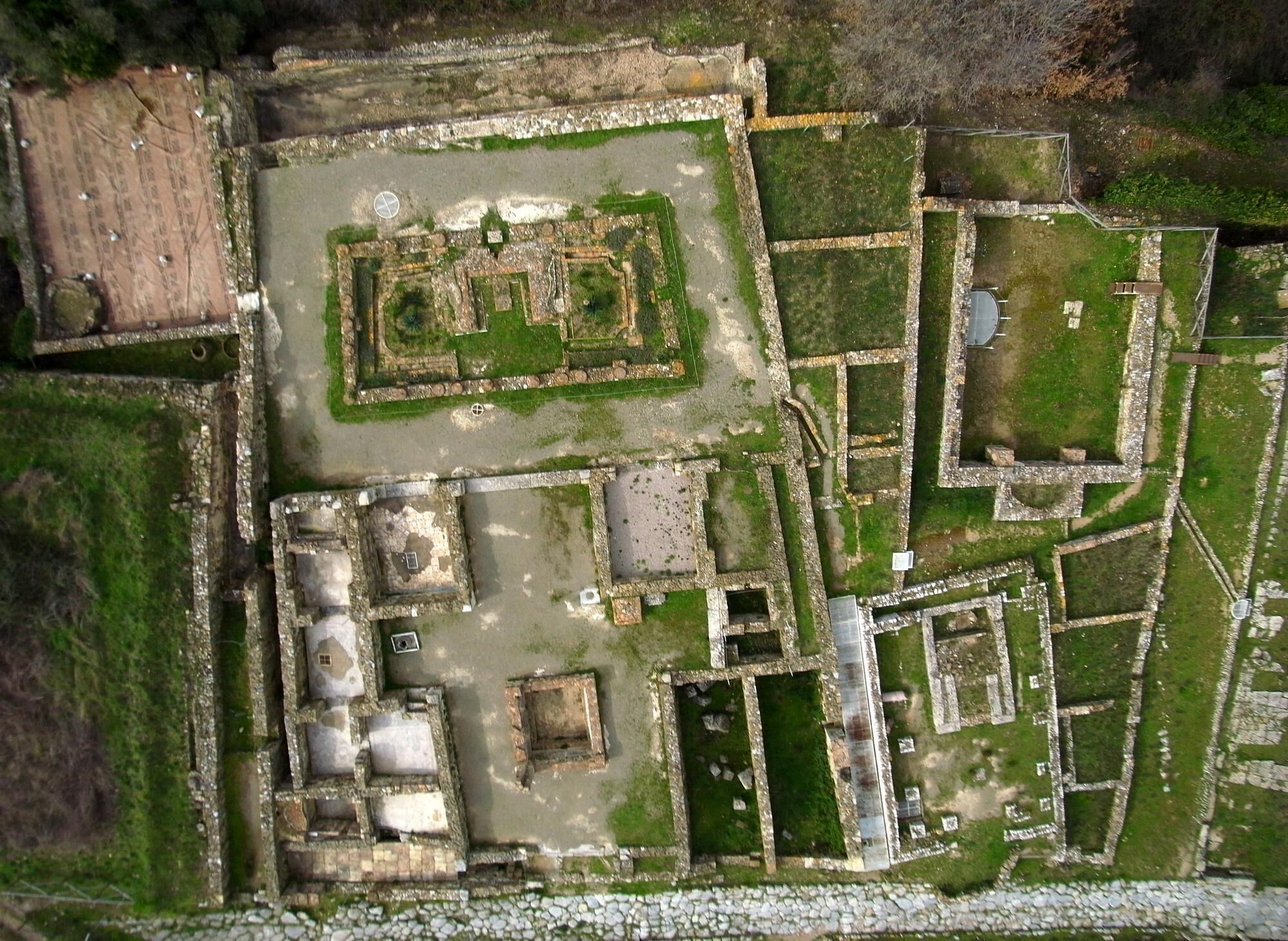 An aerial view of an ancient archaeological site with rectangular ruins, pathways, and open grassy areas.