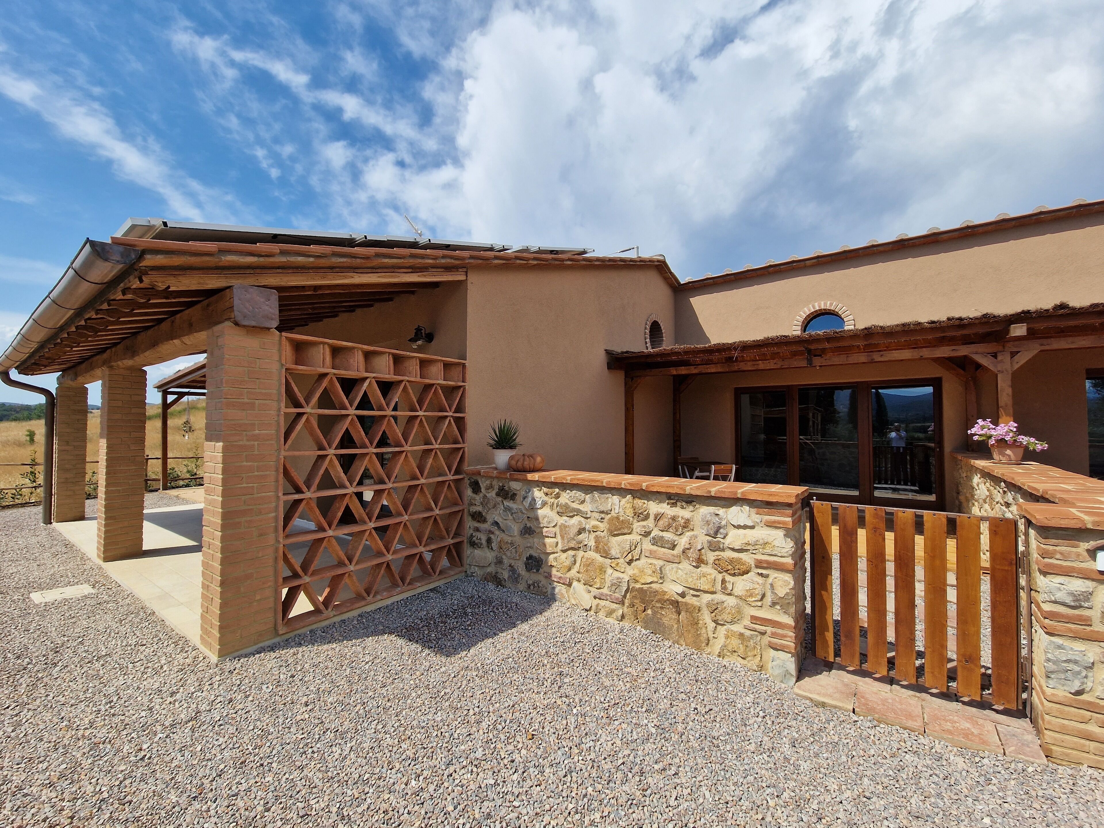 A building with a stone wall, wooden pergola, and a wooden fence.