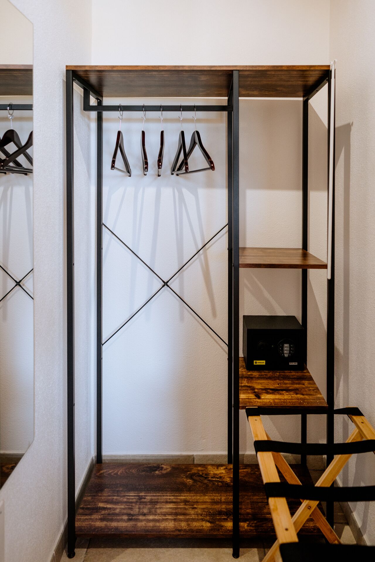 A room with a wooden floor, a metal-framed shelving unit with clothes hanging, and a black electronic device on the floor.
