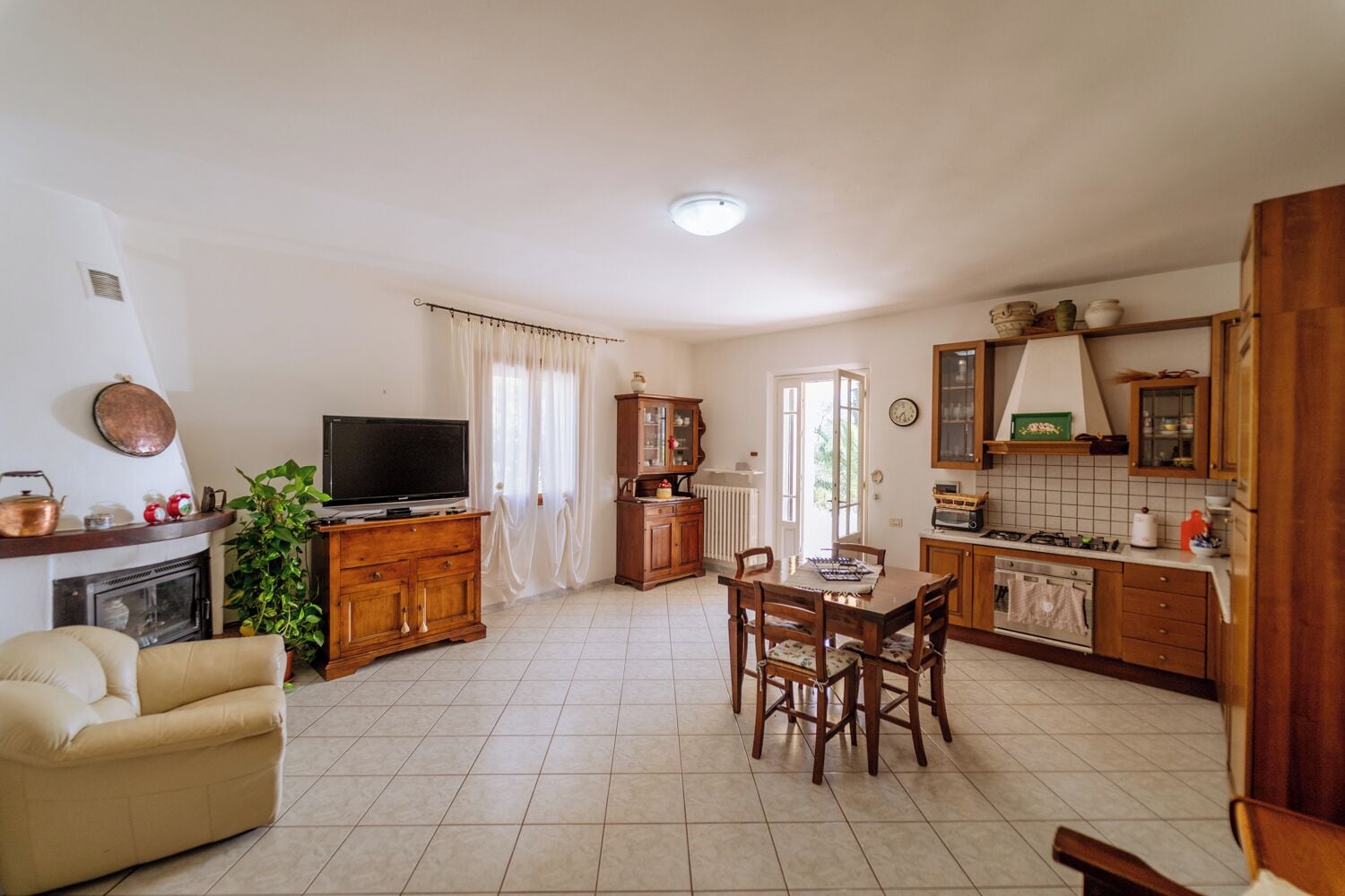 Ein gemütliches Wohnzimmer mit Kamin, Fernseher, einem Esstisch mit Stühlen und einer Küchenzeile mit Schränken und einem Fenster.