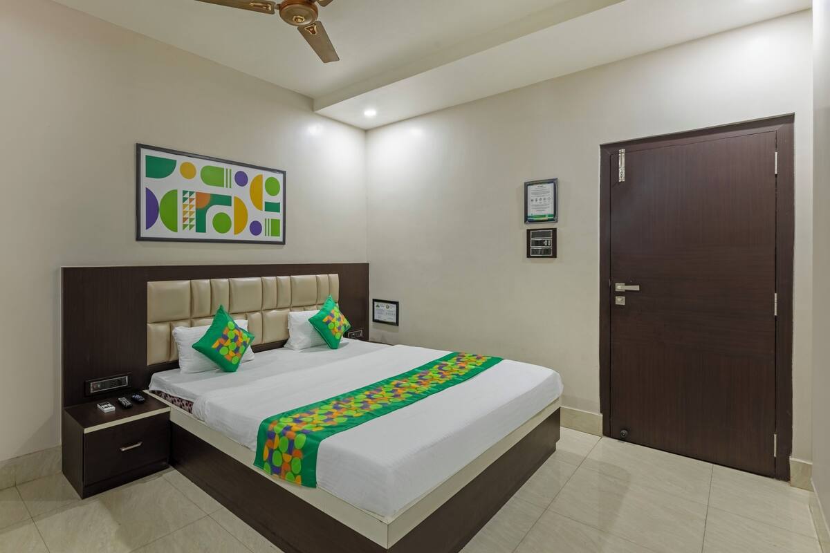 A hotel room with a bed, a nightstand, a ceiling fan, a door, and a wall-mounted artwork.