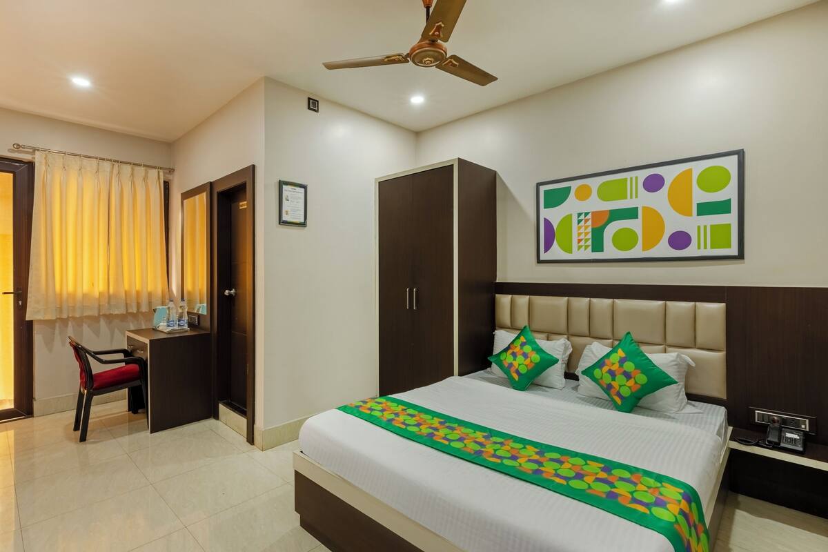 A hotel room with a bed, a desk, a wardrobe, a ceiling fan, and a wall art piece.