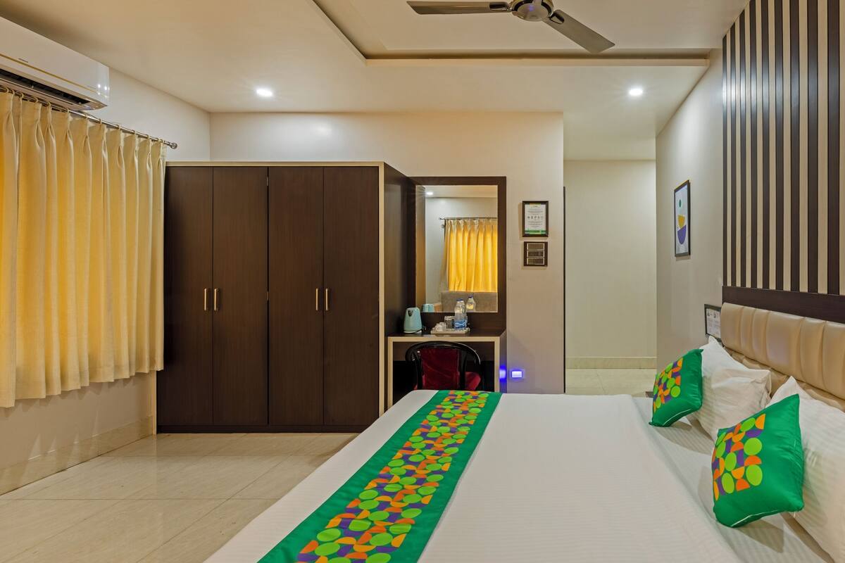 A hotel room with a large bed, a wardrobe, a bathroom with a mirror, and a ceiling fan.