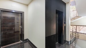Ein moderner Aufzug mit Bedienfeld, einer dunklen Holztür und einer Treppe mit Metallgeländern.