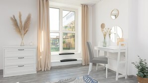 A modern bedroom with a white dresser, a desk with a chair, a large window with curtains, and a small potted plant. - Spacious Apartment in Zoliborz | Terrace | Workspace (Warszawa)