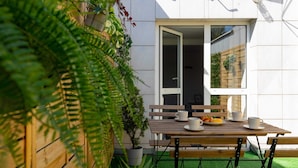 A wooden table with chairs and a potted plant in a garden area with a white wall and a window. - Spacious Apartment in Zoliborz | Terrace | Workspace (Warszawa)