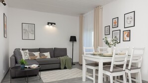 A modern living room with a grey sofa, a small black coffee table, and a dining area with white chairs and a table. - Spacious Apartment in Zoliborz | Terrace | Workspace (Warszawa)
