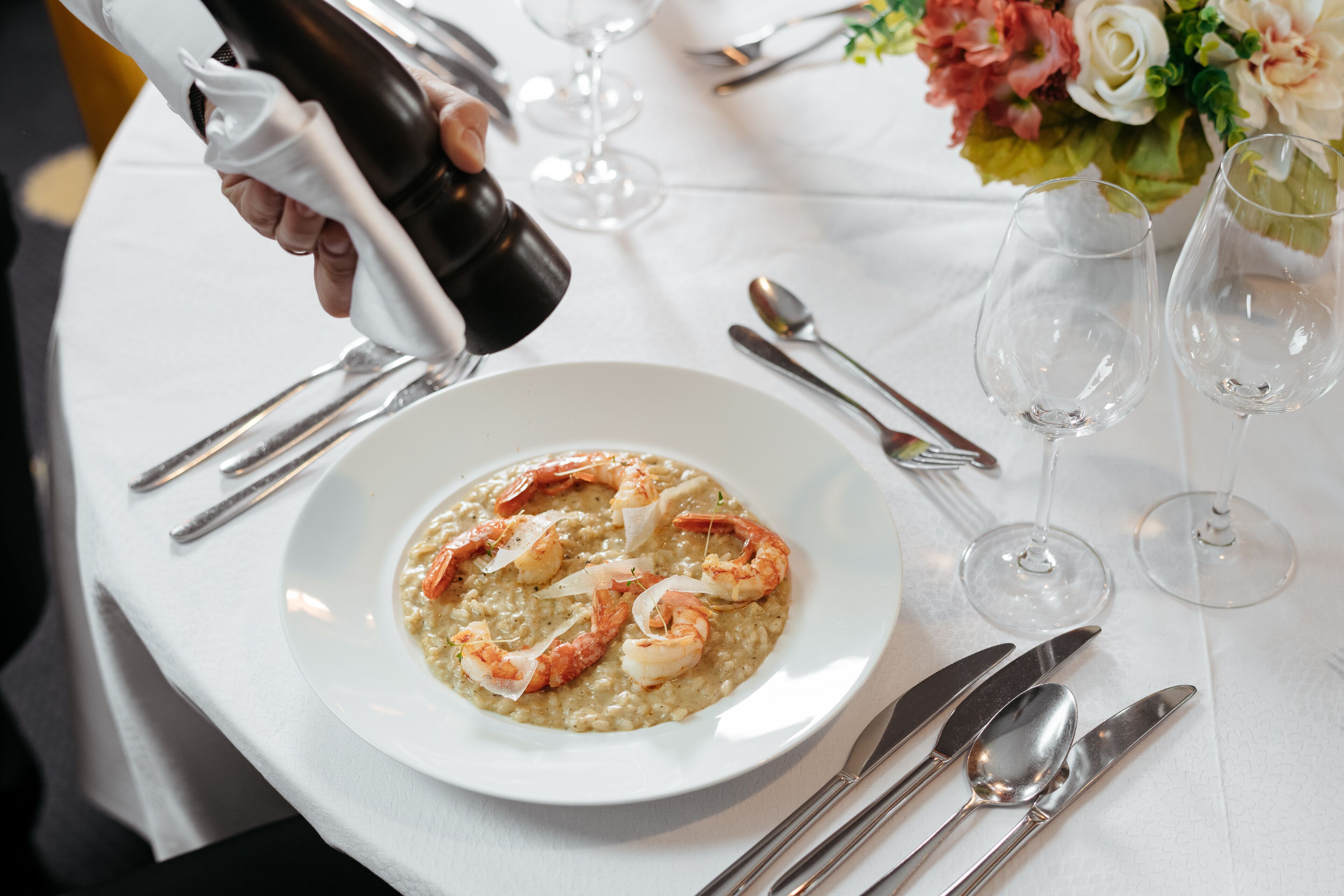 Uma mesa de jantar posta com um prato de risoto de frutos do mar, copos de vinho e talheres.
