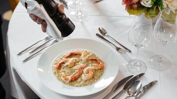 Uma mesa de jantar posta com um prato de risoto de frutos do mar, copos de vinho e talheres.