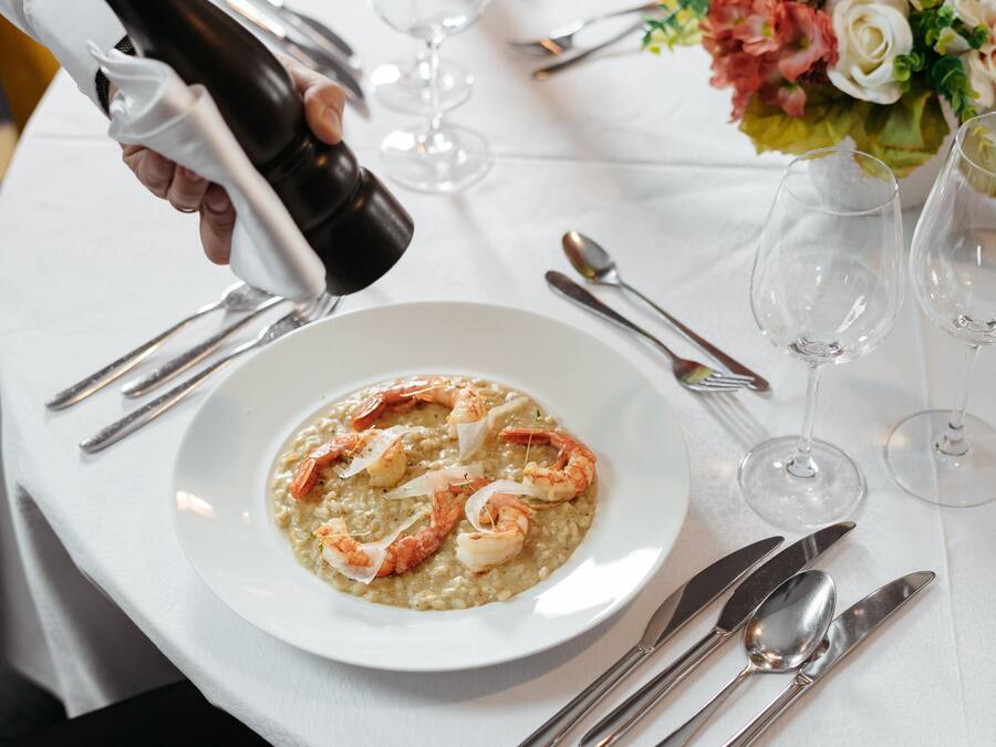 Uma mesa de jantar posta com um prato de risoto de frutos do mar, copos de vinho e talheres.