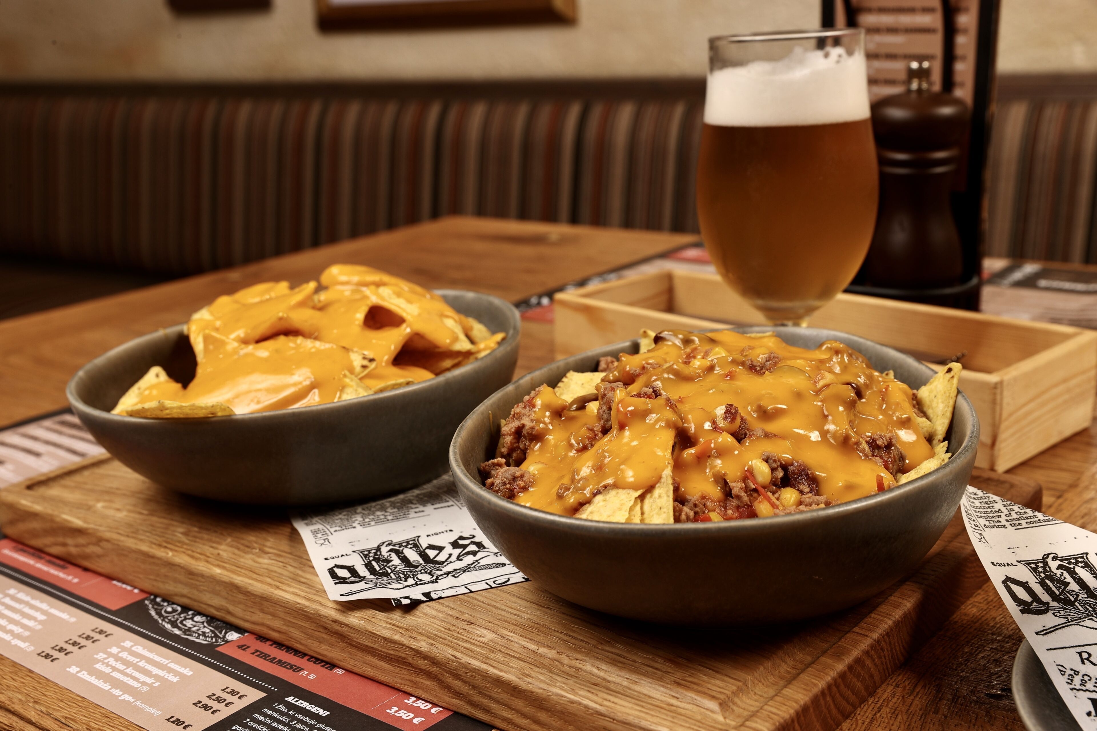Una mesa con nachos y una cerveza, además de un menú con precios.