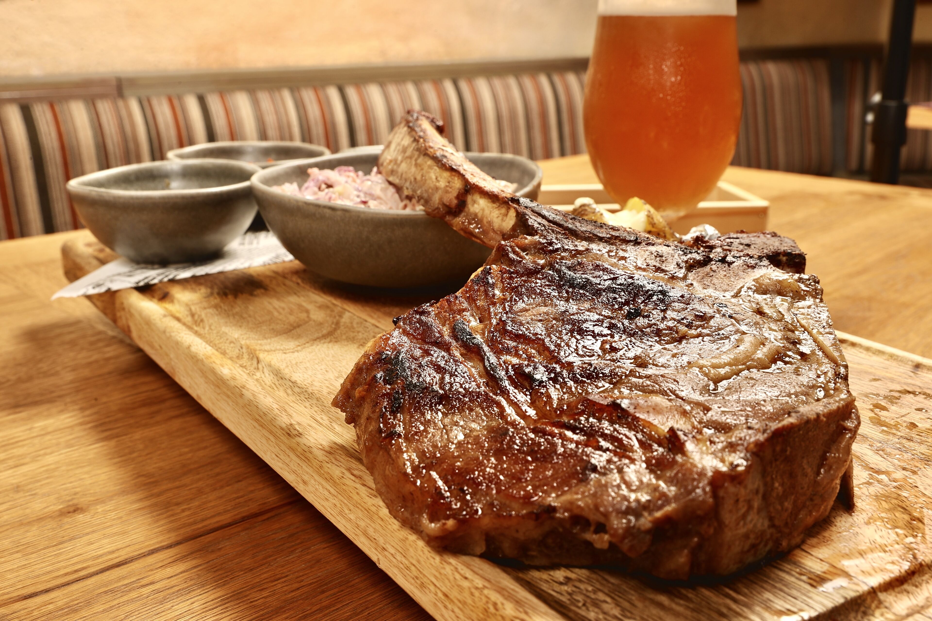 A steak with a side of condiments and a glass of beer on a wooden table.