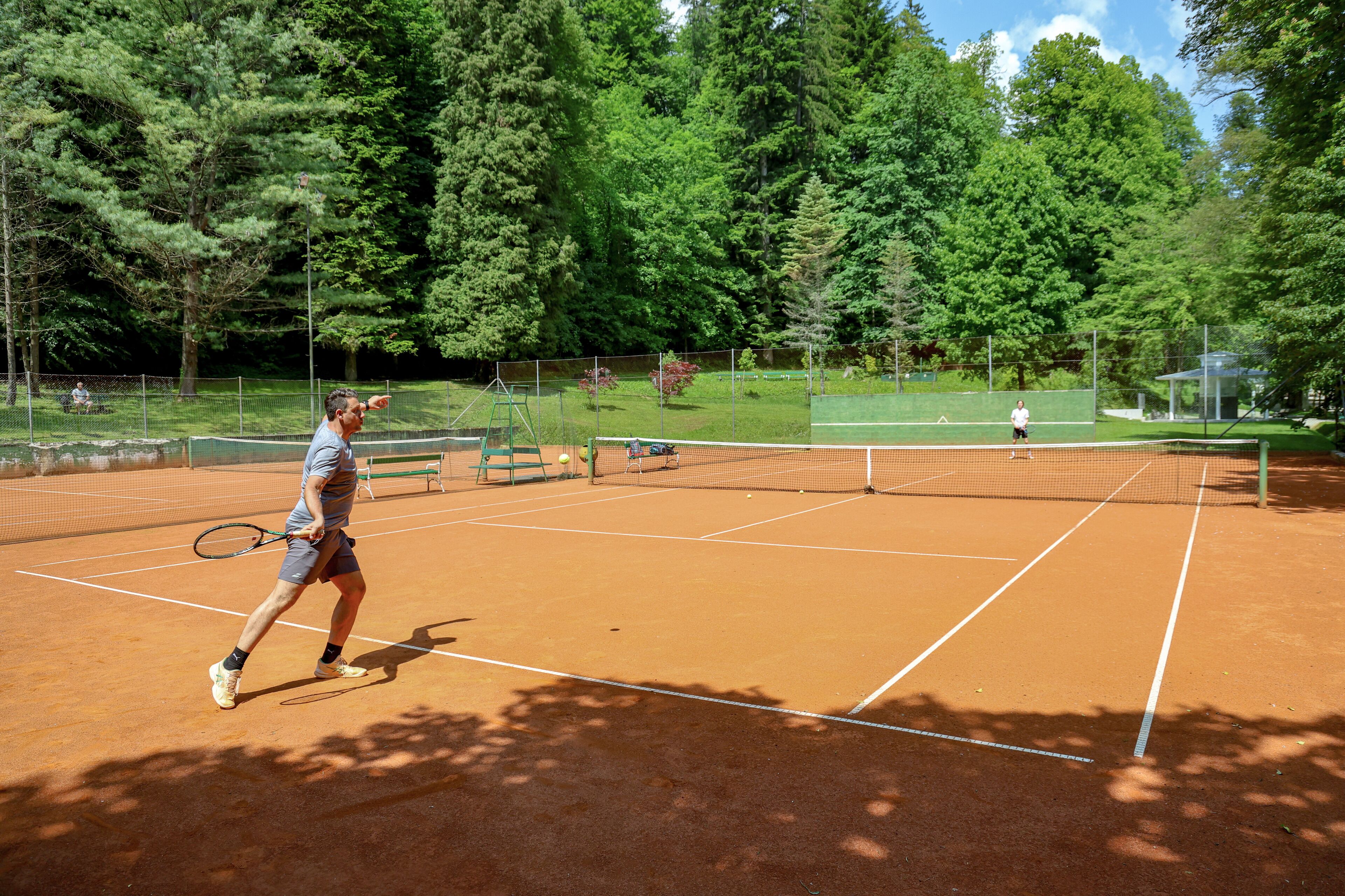 A tennis court with a net, surrounded by trees and a fence.