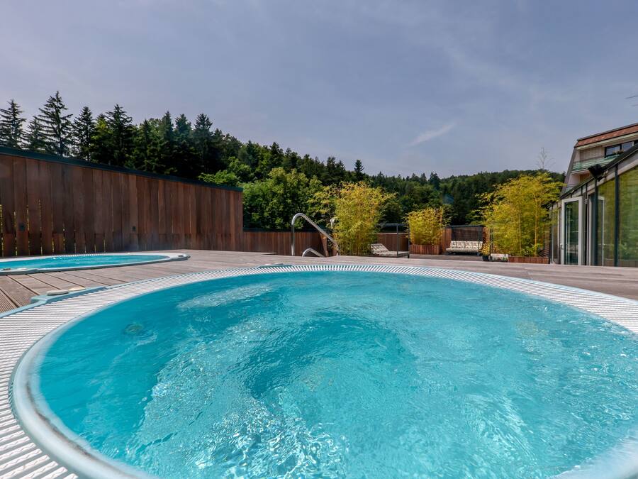 A swimming pool with a wooden deck and a view of a forested hillside.