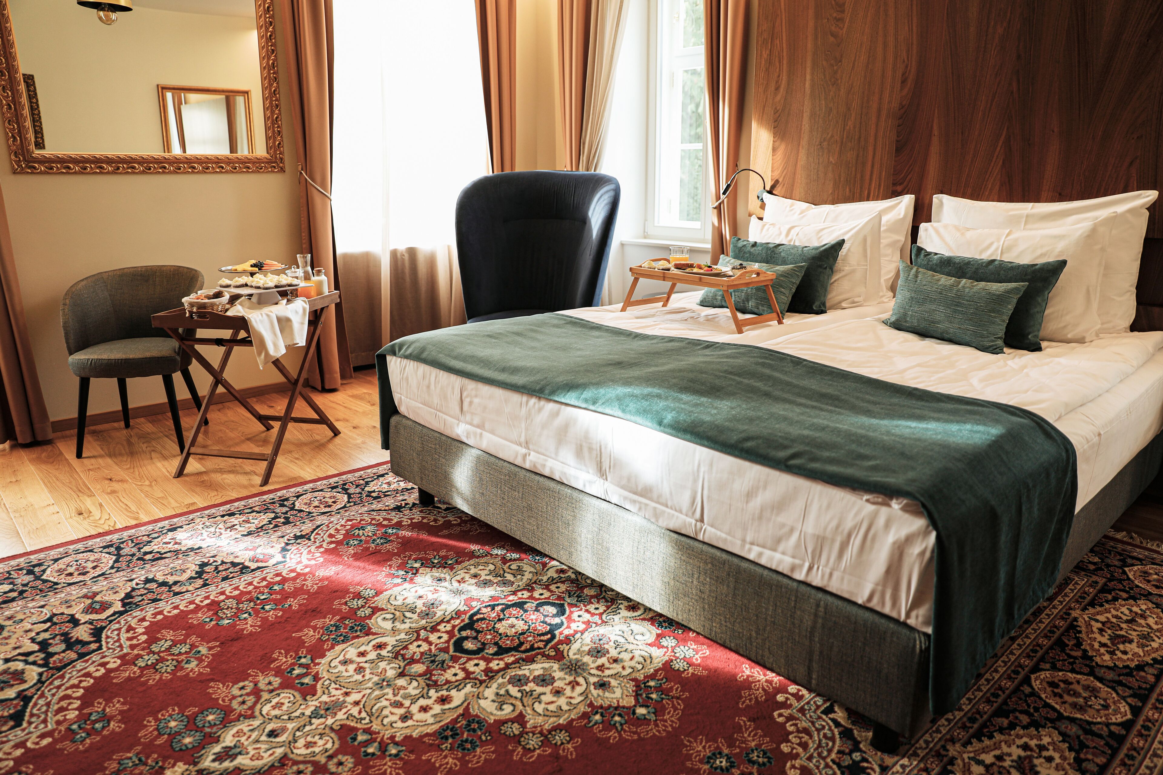 Une chambre d’hôtel avec un grand lit, un bureau avec une chaise, un miroir et une fenêtre avec des rideaux.