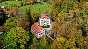 A large, multi-story hotel with a red roof, surrounded by lush greenery and hills.