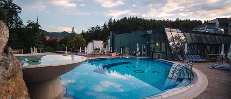 A swimming pool with a glass enclosure, surrounded by lounge chairs and a stone deck.