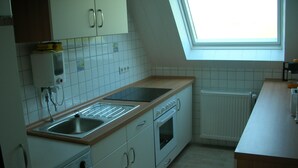 A kitchen with white cabinets, a built-in oven, a microwave, a sink, and a window above the countertop. - Beautiful fine apartment with garden, meadow, view of water and land (Dornummersiel/Dornum)