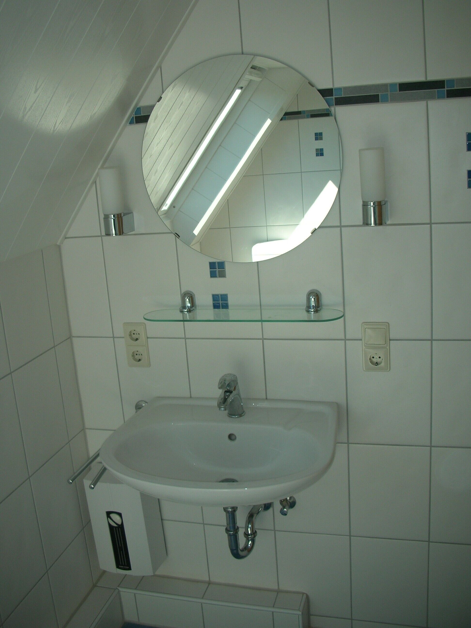 Une salle de bain avec un lavabo blanc, un miroir et une étagère en verre.