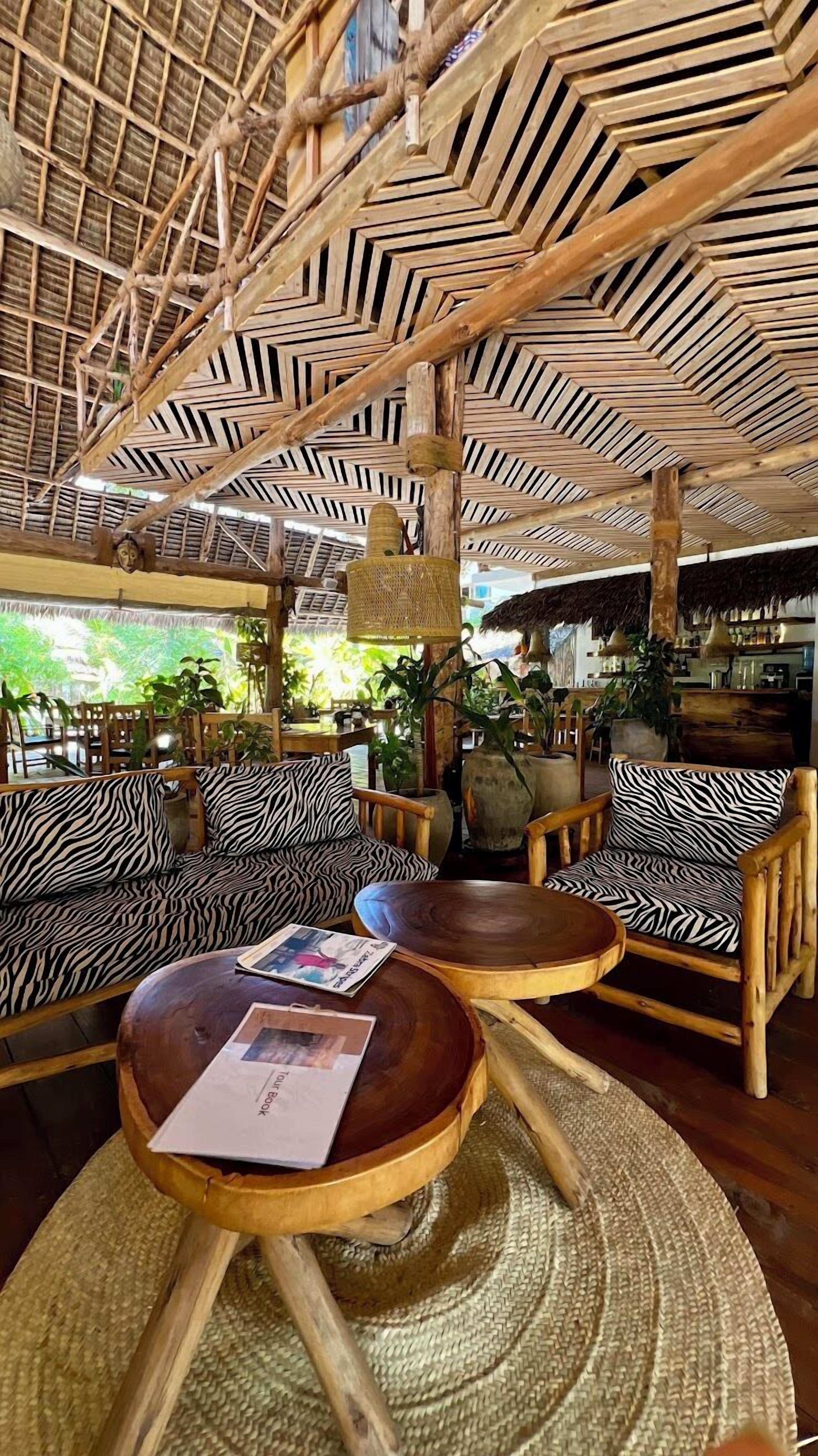 A thatched-roof outdoor seating area with wooden furniture and woven mats.