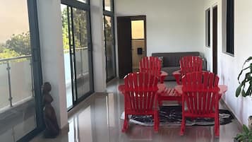 A spacious room with a modern design, featuring a dining area with red chairs and a table, large windows, and a view of the outdoors.