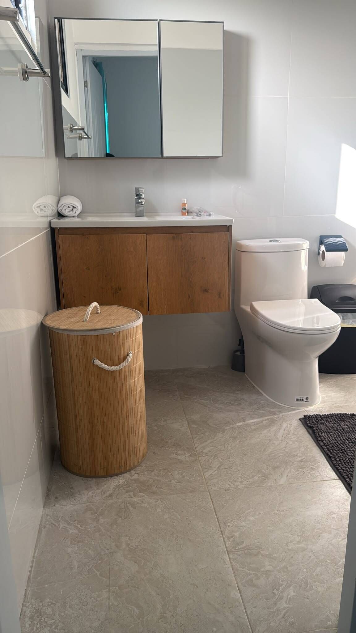 A bathroom with a toilet, sink, mirror, and a wooden trash bin.
