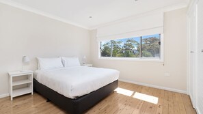 Una camera da letto con un letto, due comodini, una finestra vista alberi e una porta.