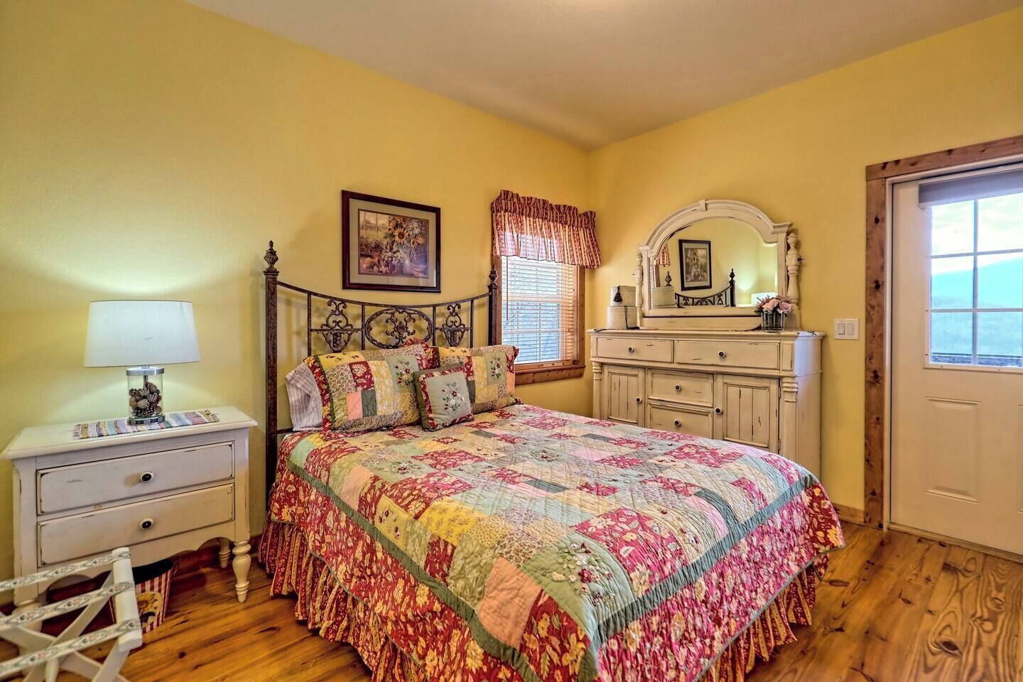 Een slaapkamer met een houten bed, een nachtkastje met lamp, een dressoir en een spiegel.